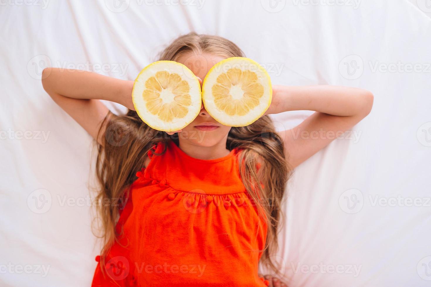 Little girl covering eyes with lemon halves near eyes photo