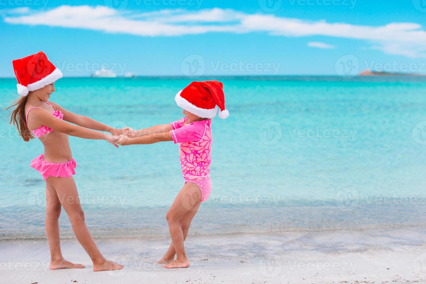 Little adorable girls in Santa hats during beach vacation have fun together photo