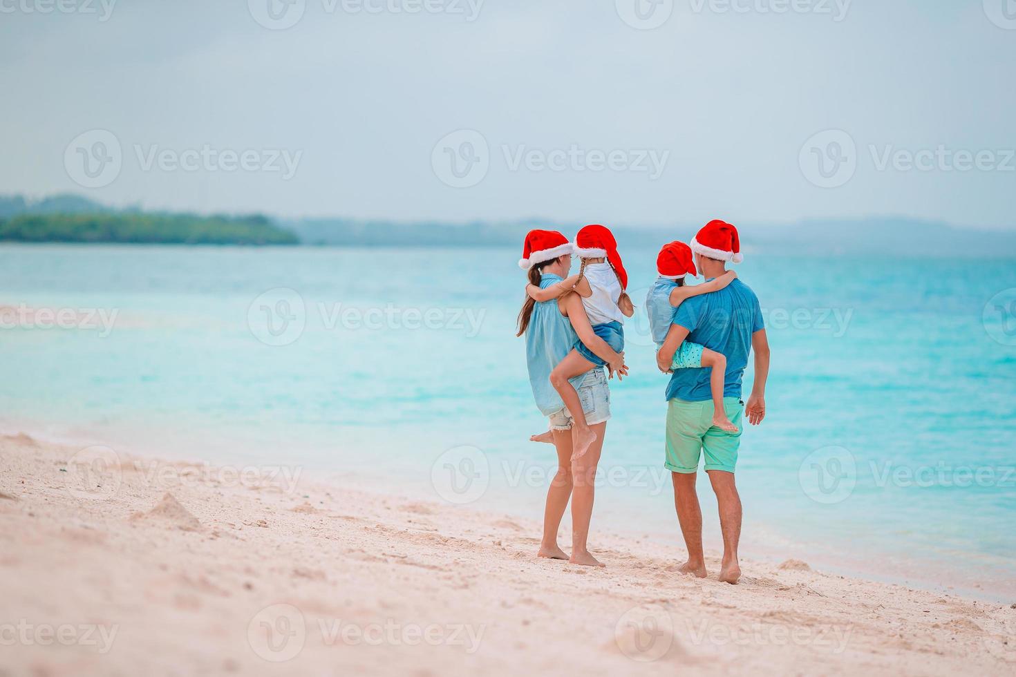 familia feliz con sombreros rojos de santa en una playa tropical celebrando las vacaciones de navidad foto