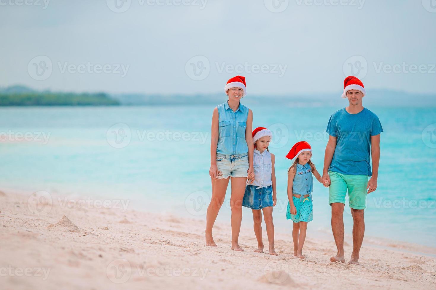 Happy family in red Santa hats on a tropical beach celebrating Christmas vacation photo