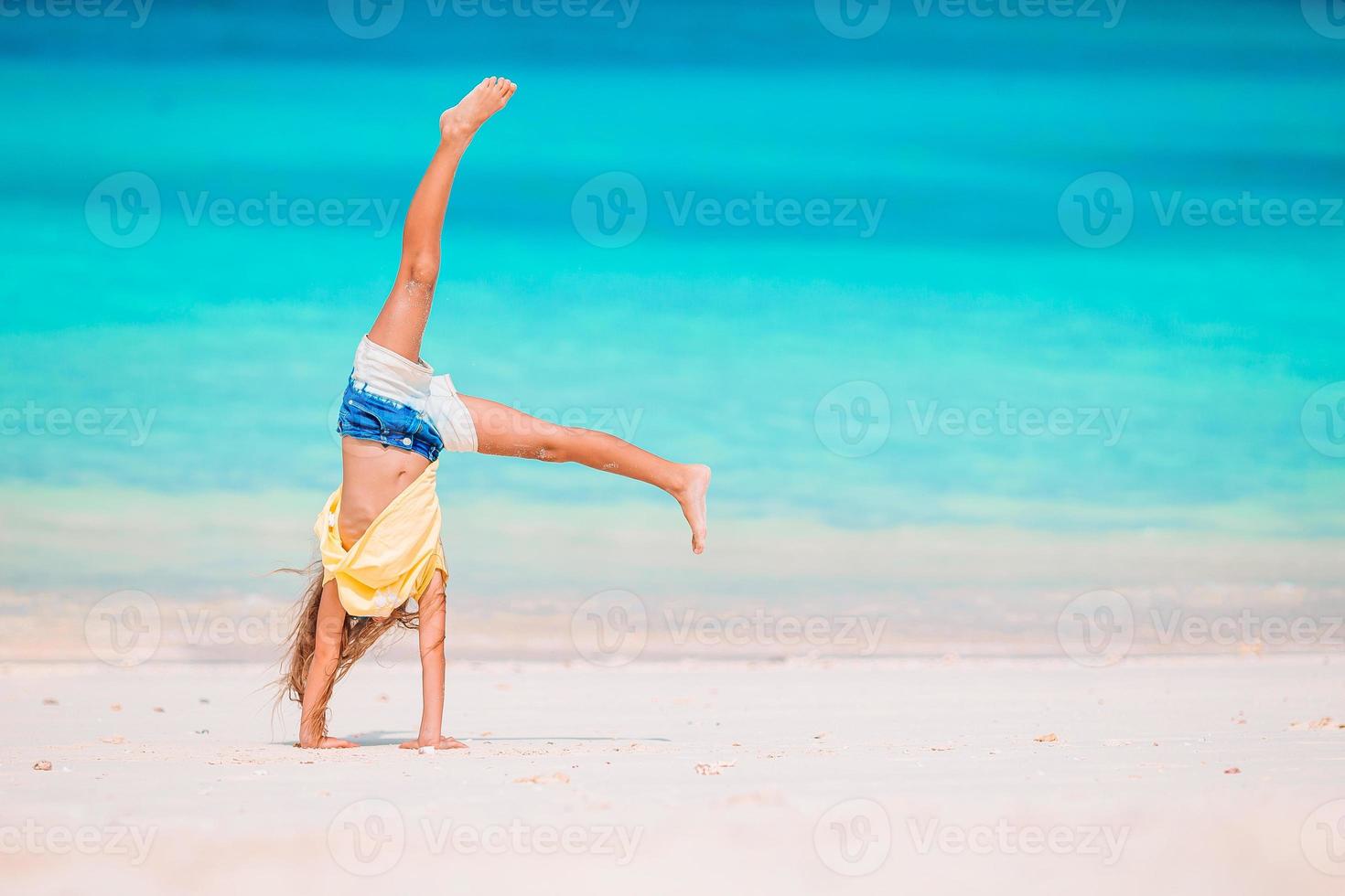 Active little girl at beach having a lot of fun. Cute kid making sporty exercises on the seashore photo