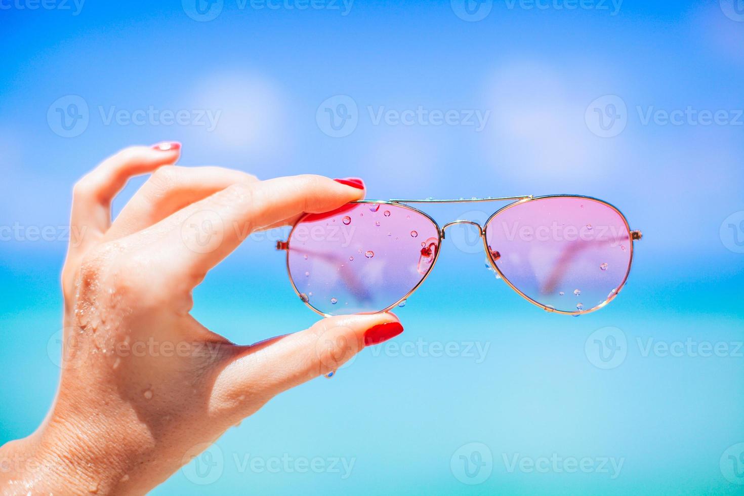 womans hand holding sunglasses on tropical beach photo