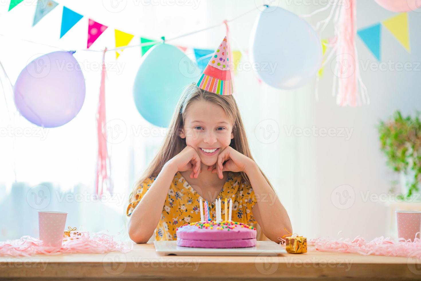 la chica caucásica sonríe soñadoramente y mira el pastel de arco iris de cumpleaños. fondo colorido festivo con globos. concepto de fiesta y deseos de cumpleaños. foto