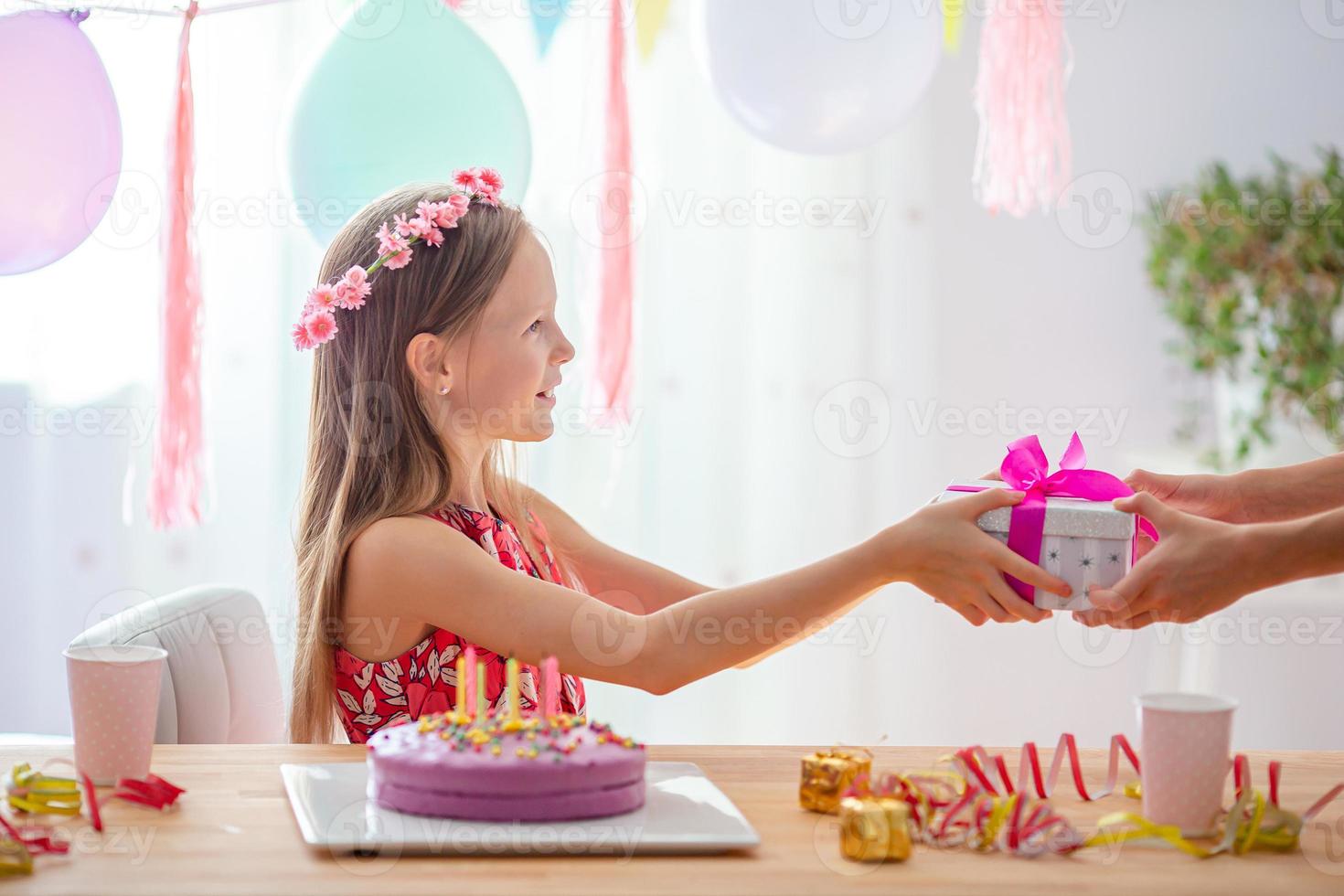 Caucasian girl is dreamily smiling and looking at birthday rainbow cake. Festive colorful background with balloons. Birthday party and wishes concept. photo