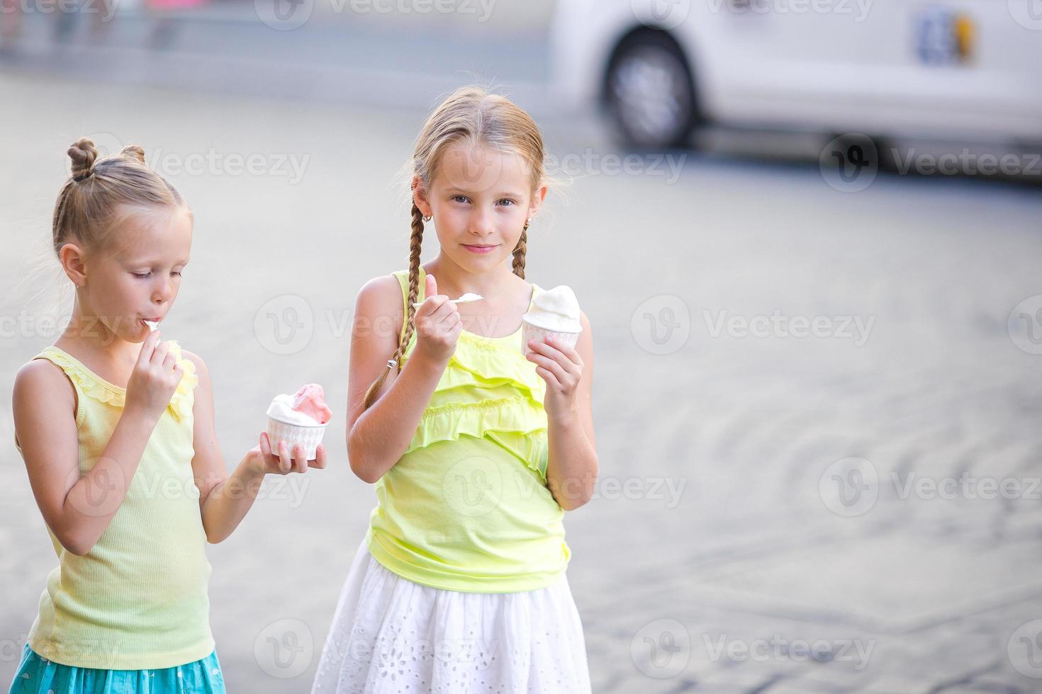 Happy little girls eating ice-creamin open-air cafe. People, children, friends and friendship concept photo