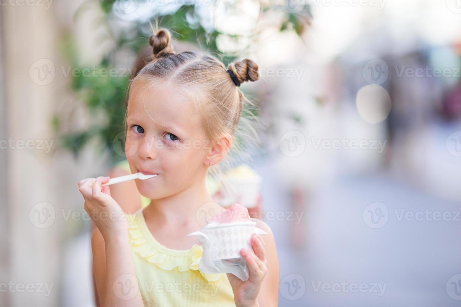 Adorable little girl eating ice-cream outdoors at summer. Cute kid enjoying real italian gelato near Gelateria in Rome photo