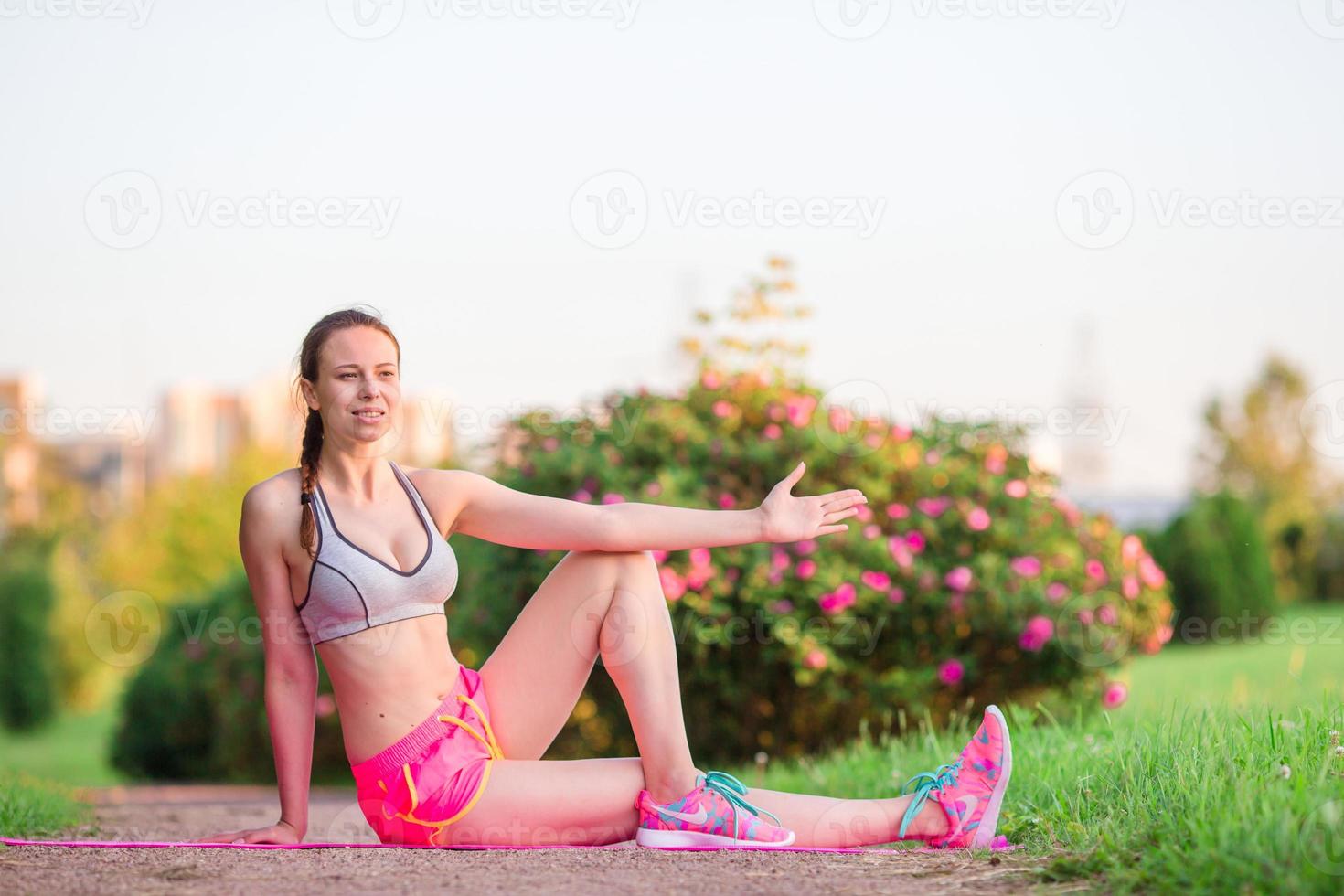 joven mujer sonriente haciendo ejercicios deportivos al aire libre. modelo de fitness femenino entrenando afuera en el parque. estilo de vida de fitness de bienestar saludable. foto