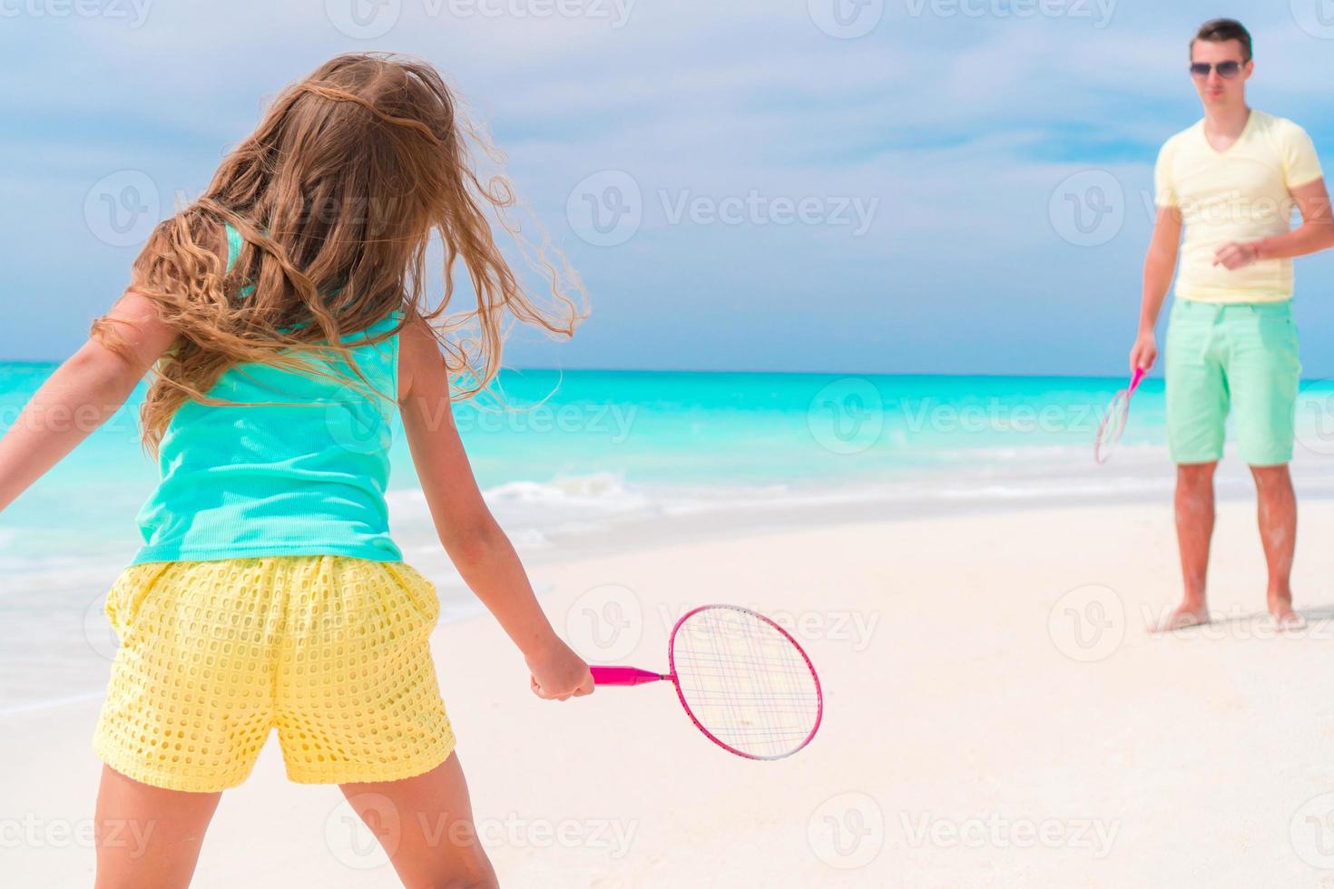 Little girl playing beach tennis on vacation with dad photo