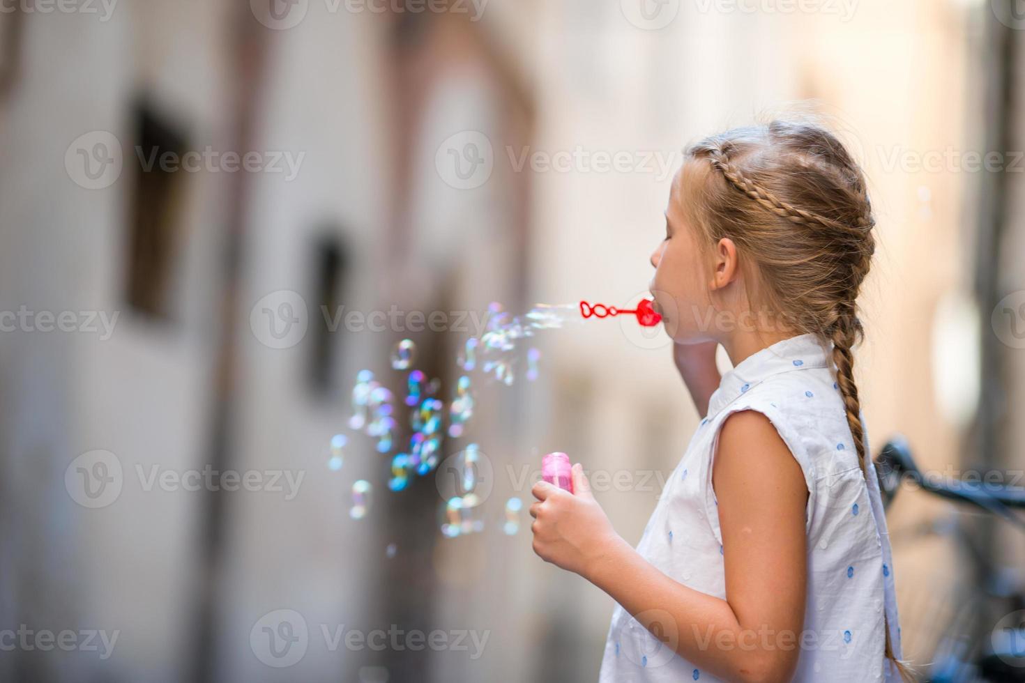 Adorable little girl outdoors blowing soap bubbles in european city. Portrait of caucasian kid enjoy summer vacation in Italy photo