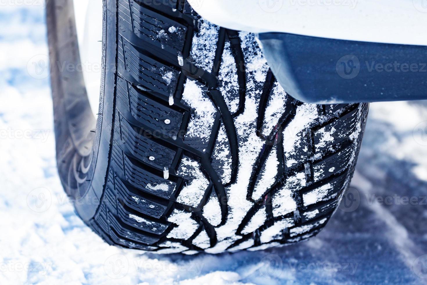 Closeup shot of automobile studded tire covered with snow at winter snowy road photo