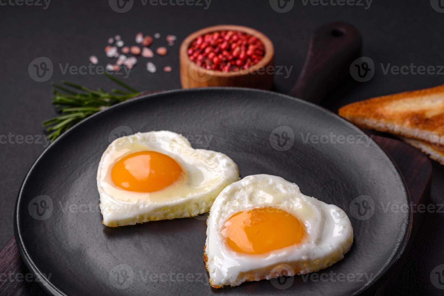 Two heart-shaped fried eggs on a black ceramic plate on a dark concrete background photo