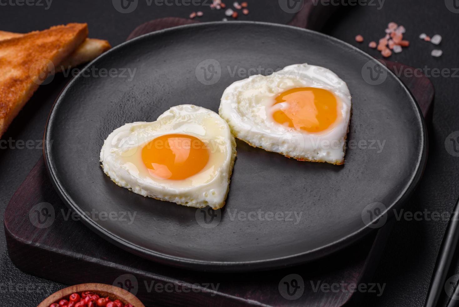 Two heart-shaped fried eggs on a black ceramic plate on a dark concrete background photo