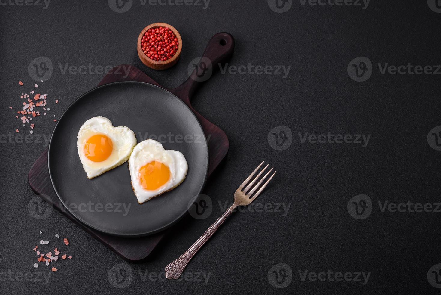 Two heart-shaped fried eggs on a black ceramic plate on a dark concrete background photo