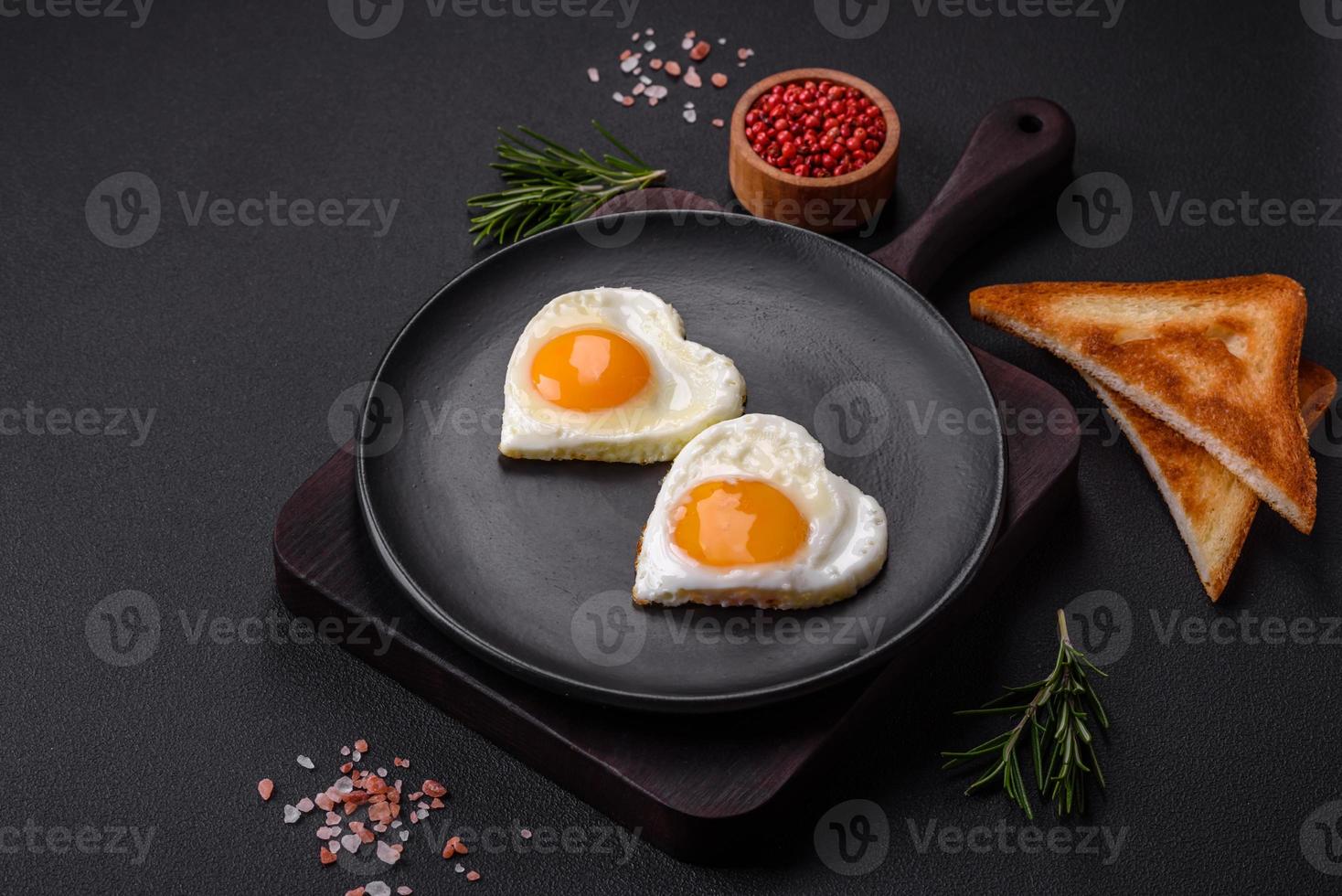 Two heart-shaped fried eggs on a black ceramic plate on a dark concrete background photo