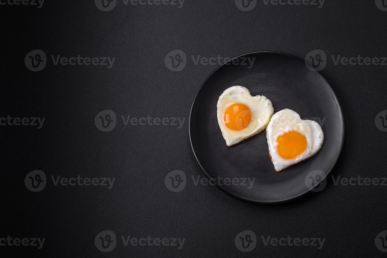 Two heart-shaped fried eggs on a black ceramic plate on a dark concrete background photo