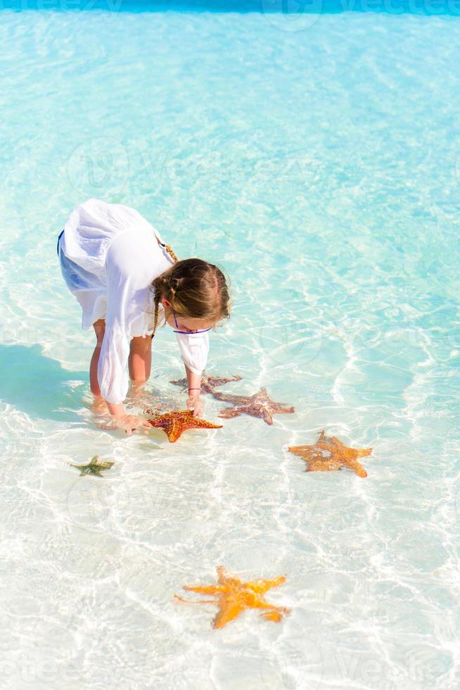 Adorable little girl with starfishes in water at clear water photo