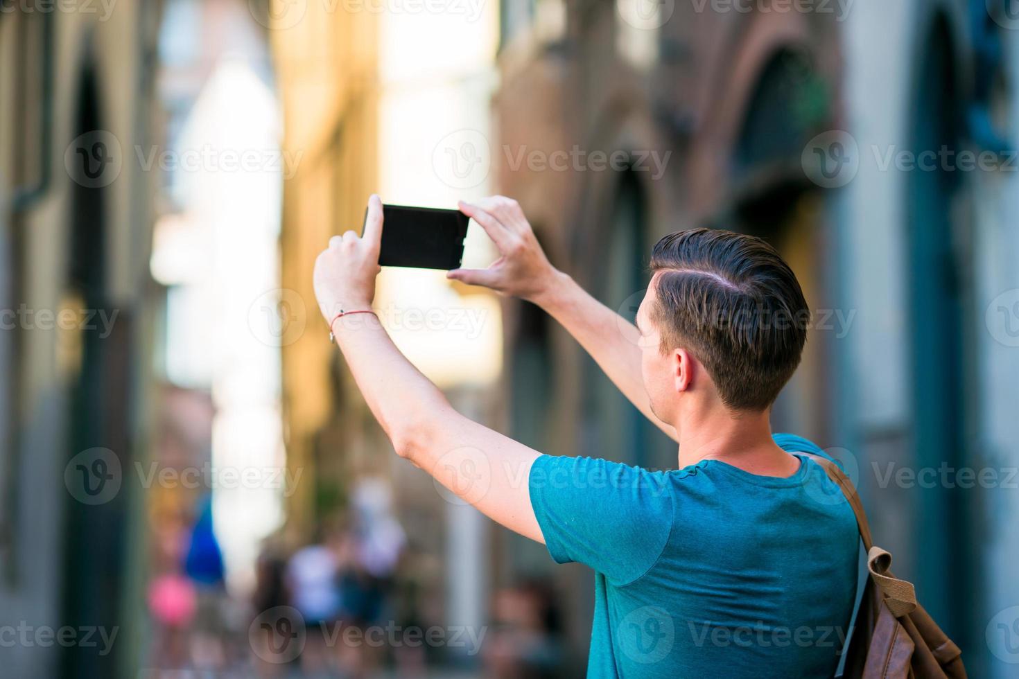 Caucasian tourist with smartphone in hands walking along the narrow italian streets in Rome. Young urban boy on vacation exploring european city photo