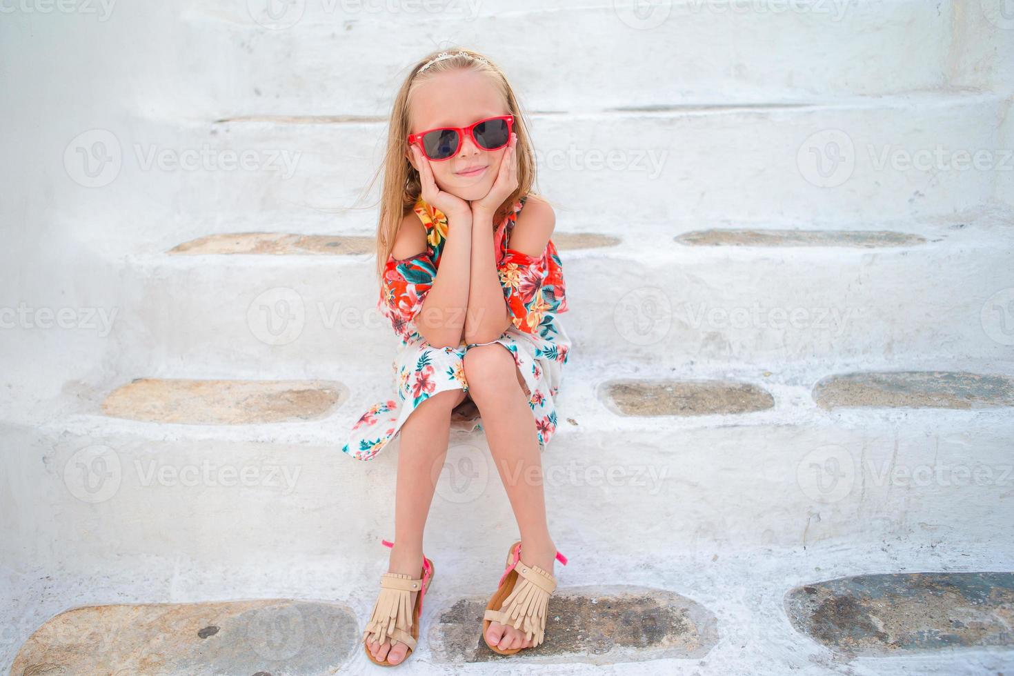 Little girl on stairs in old streets an Mykonos. Kid at street of typical greek traditional village with white walls and colorful doors on Mykonos Island, in Greece photo