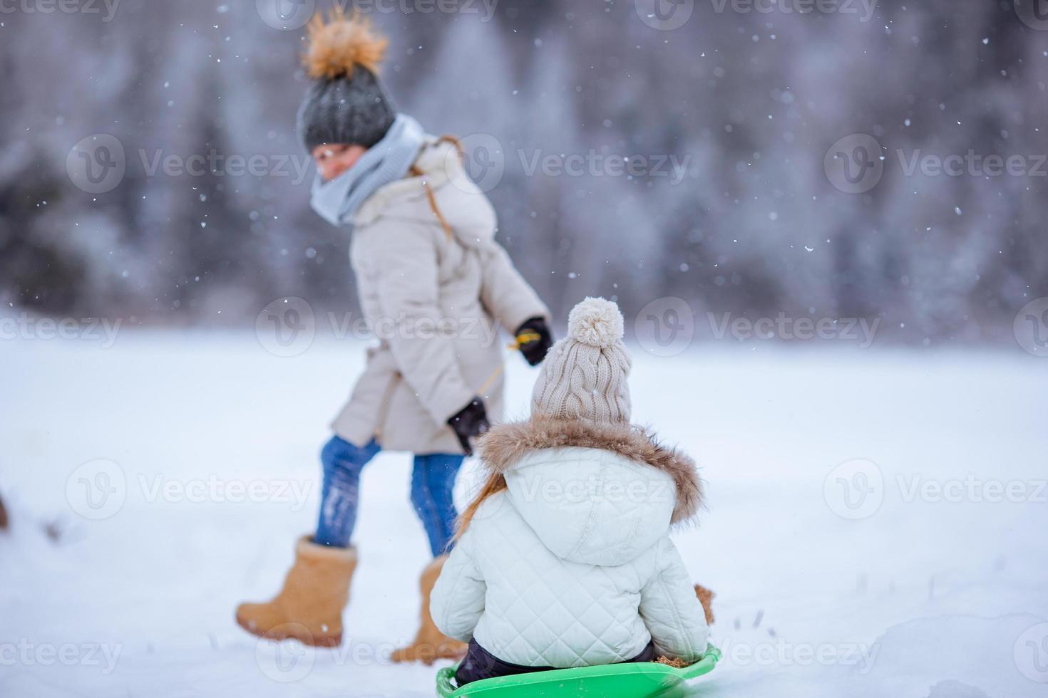 Adorable little happy girls sledding in winter snowy day. photo