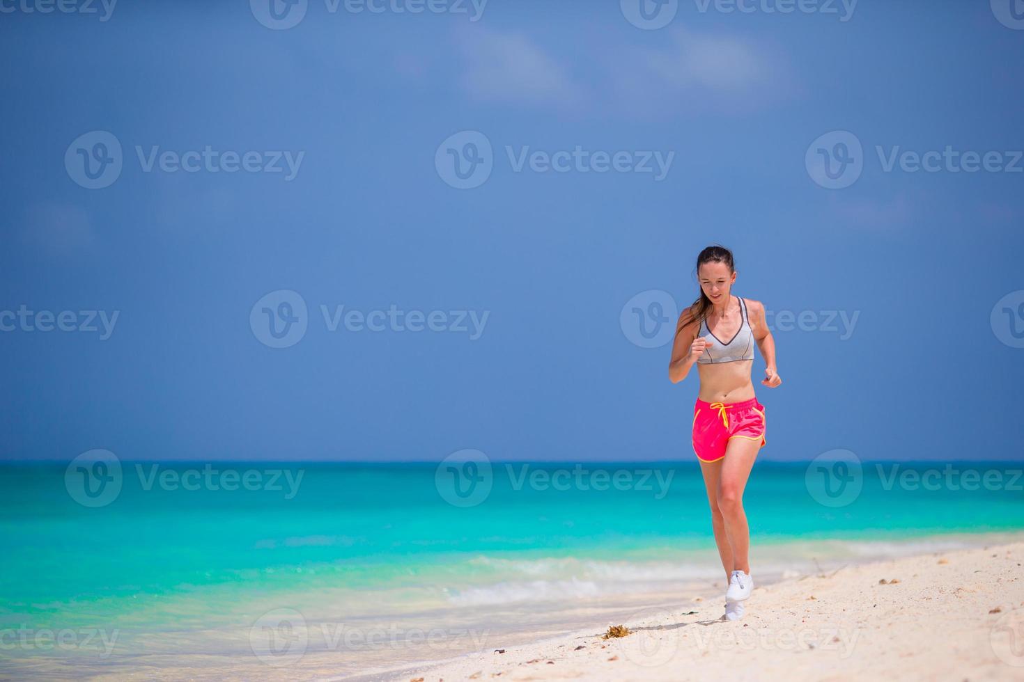 Colocar joven corriendo a lo largo de la playa tropical en su ropa deportiva foto