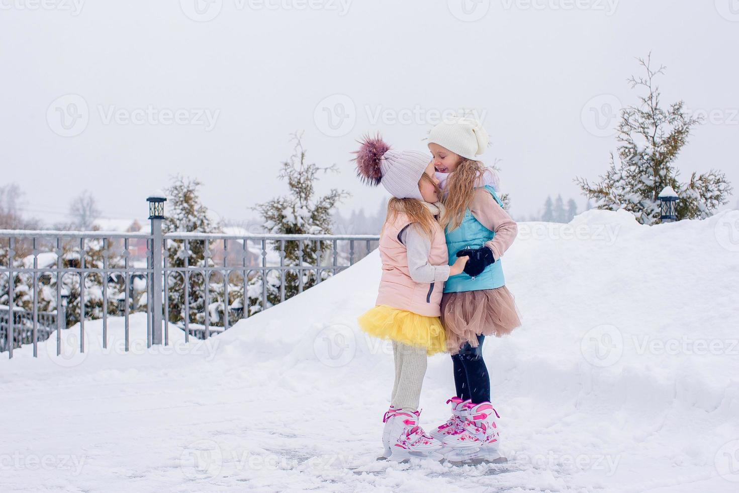 Adorable girls skating on ice rink outdoors in winter snow day photo