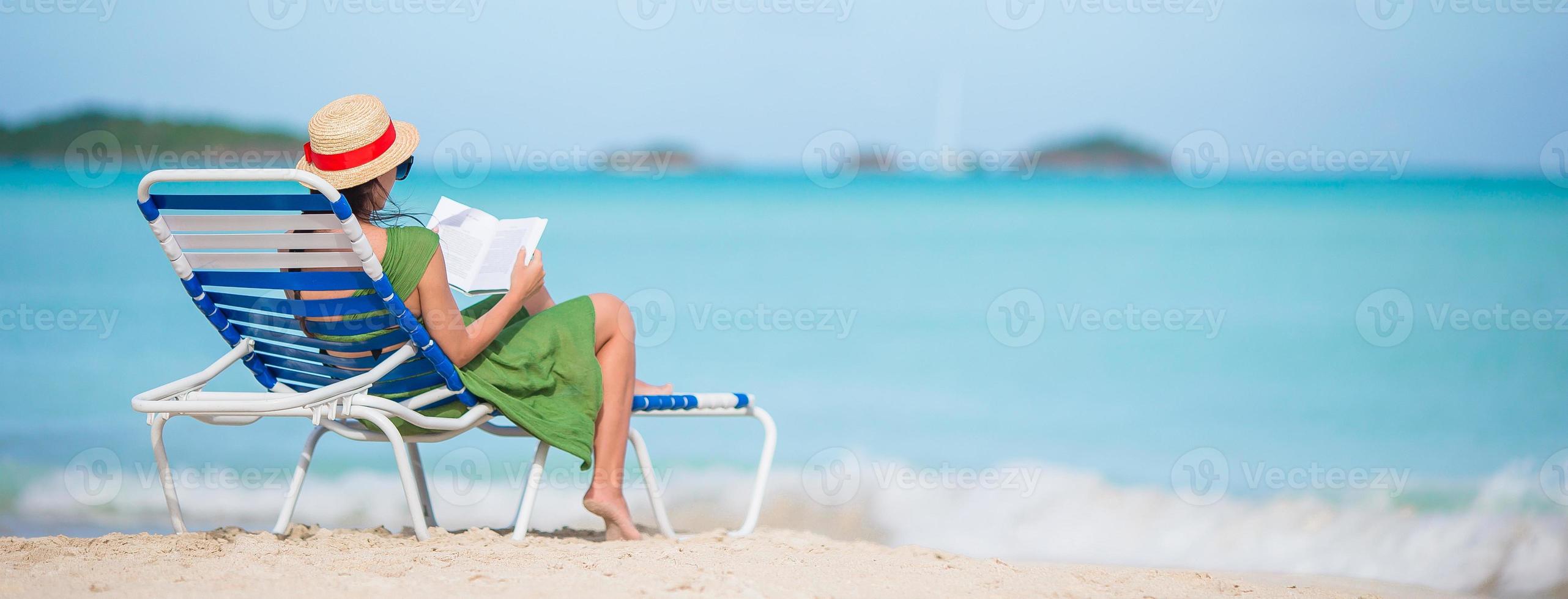 Young woman reading book on chaise-lounge on the beach photo