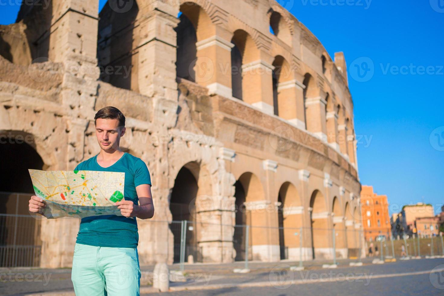 chico feliz con mapa frente al coliseo. joven buscando el fondo de la atracción la famosa zona de roma, italia foto