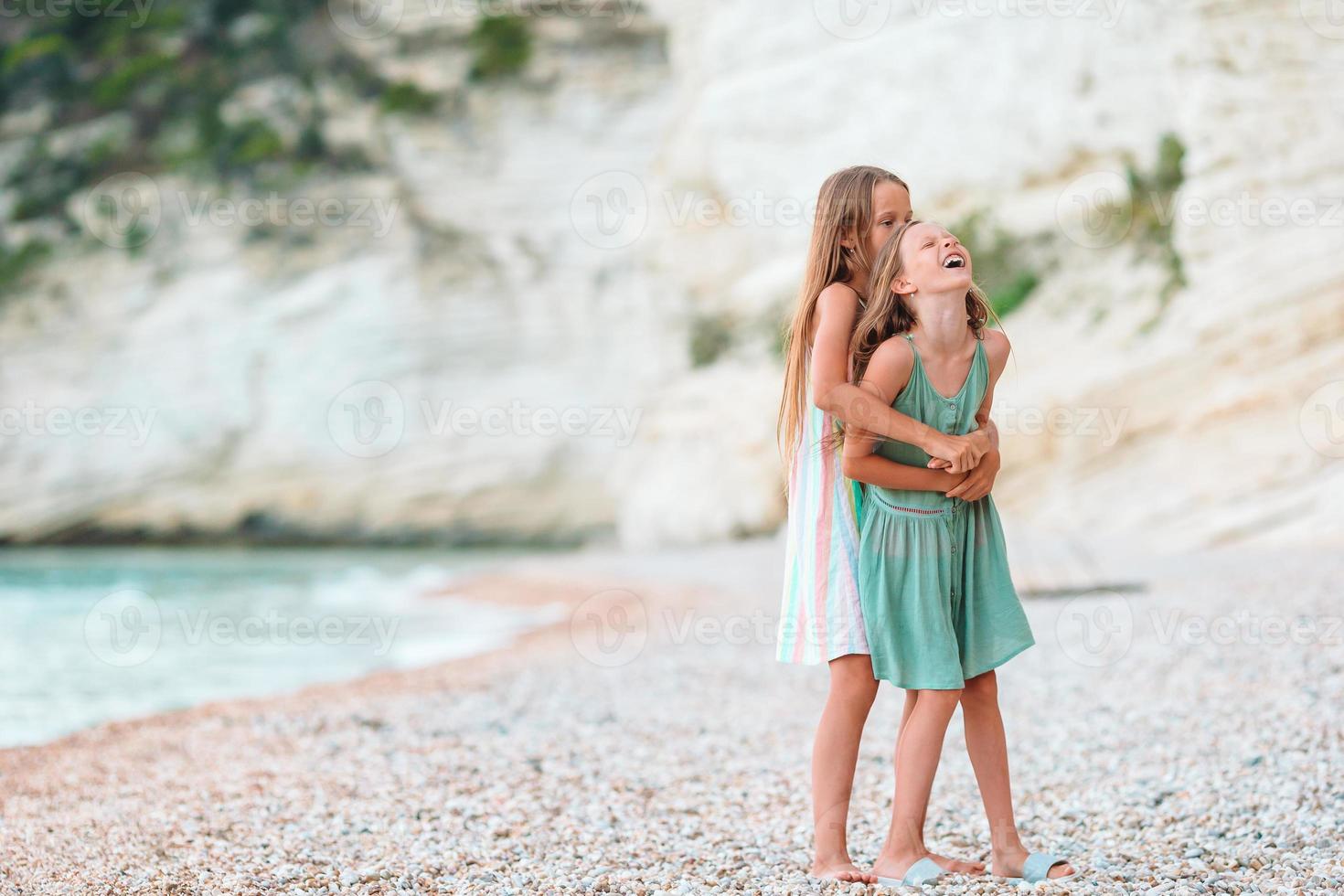 Little happy funny girls have a lot of fun at tropical beach playing together. Sunny day with rain in the sea photo