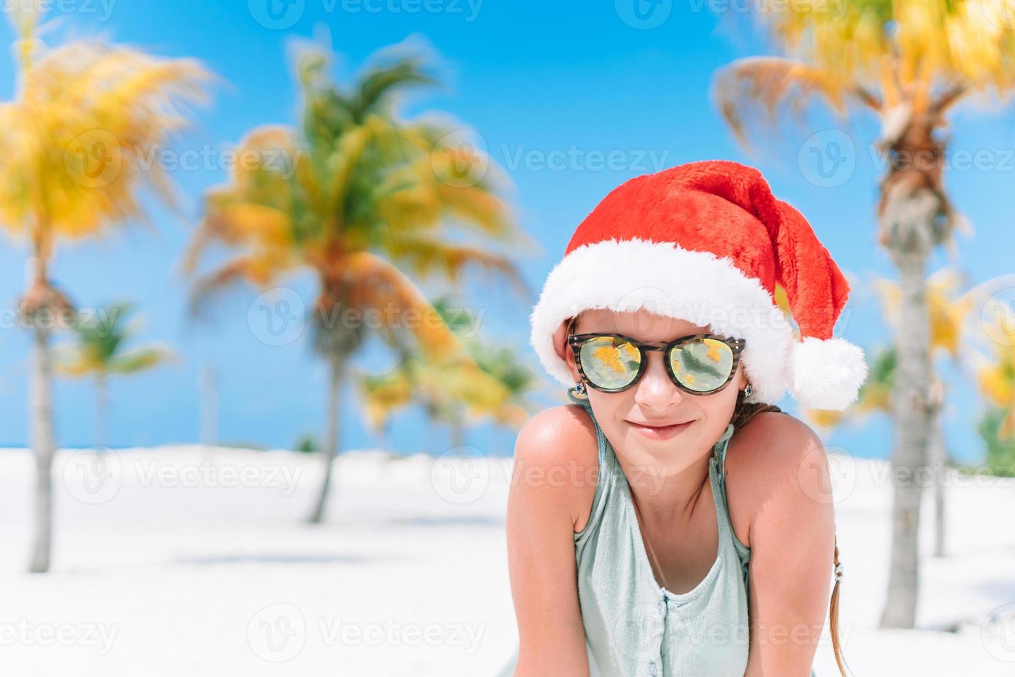 adorable niña con sombrero de santa durante las vacaciones navideñas en la playa foto