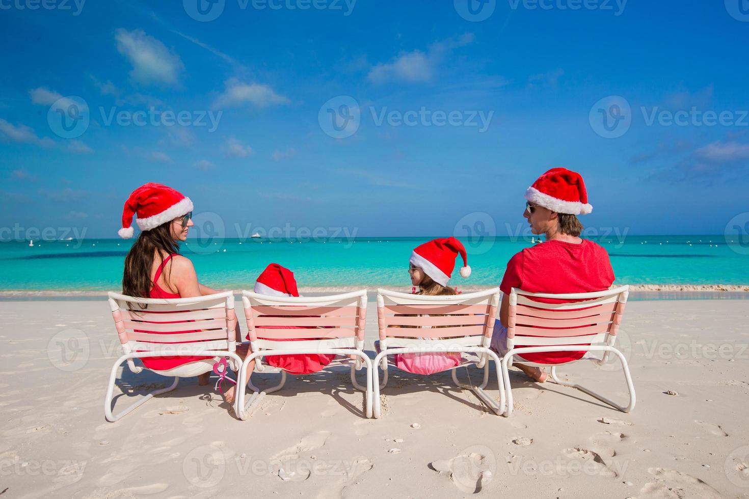 Happy family of four in Christmas Hats on white beach photo