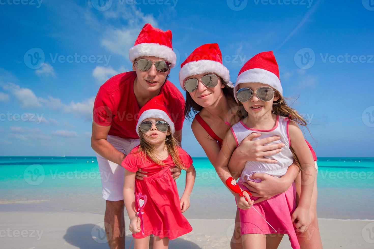 Happy family of four in Christmas Hats on white beach photo