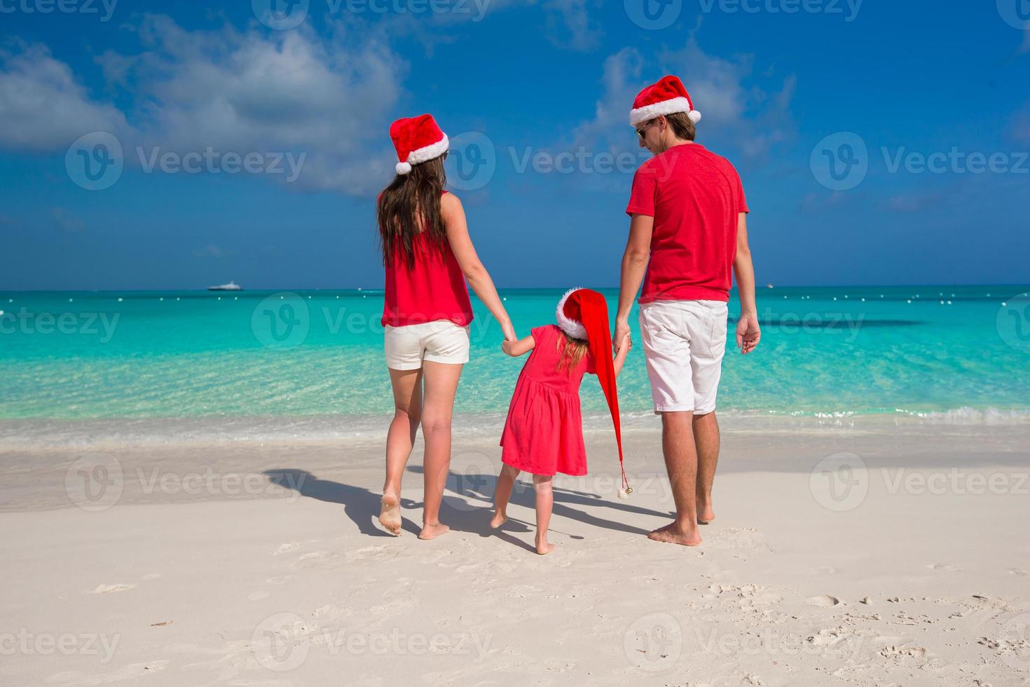 familia feliz con sombreros de navidad divirtiéndose en la playa blanca foto