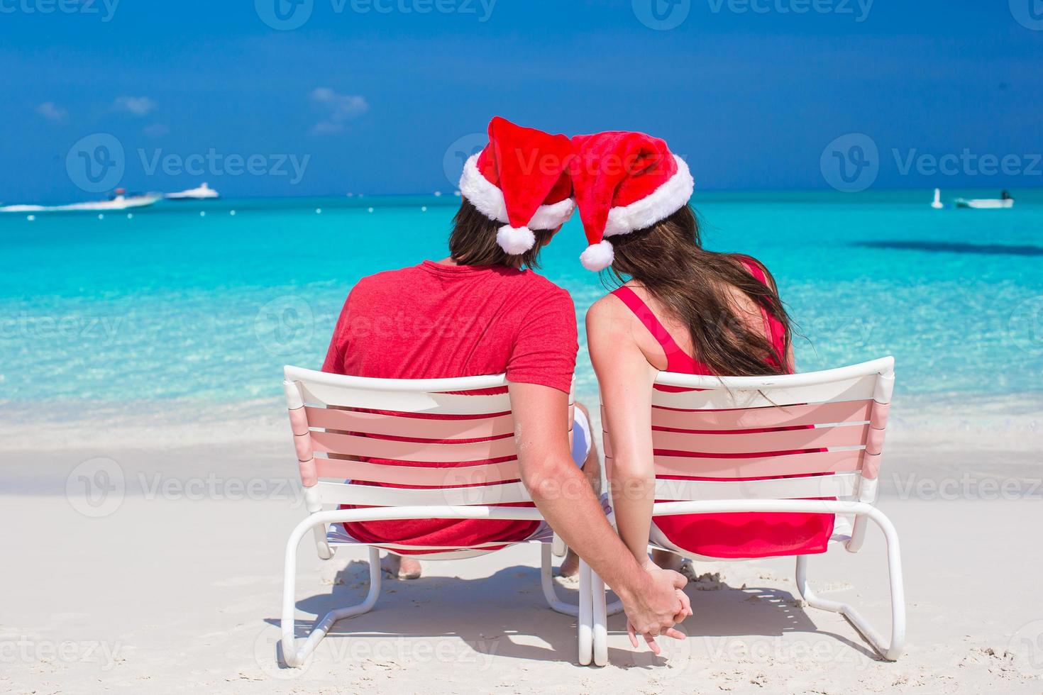 Back view of young couple in red Santa Hats sitting on beach chairs photo