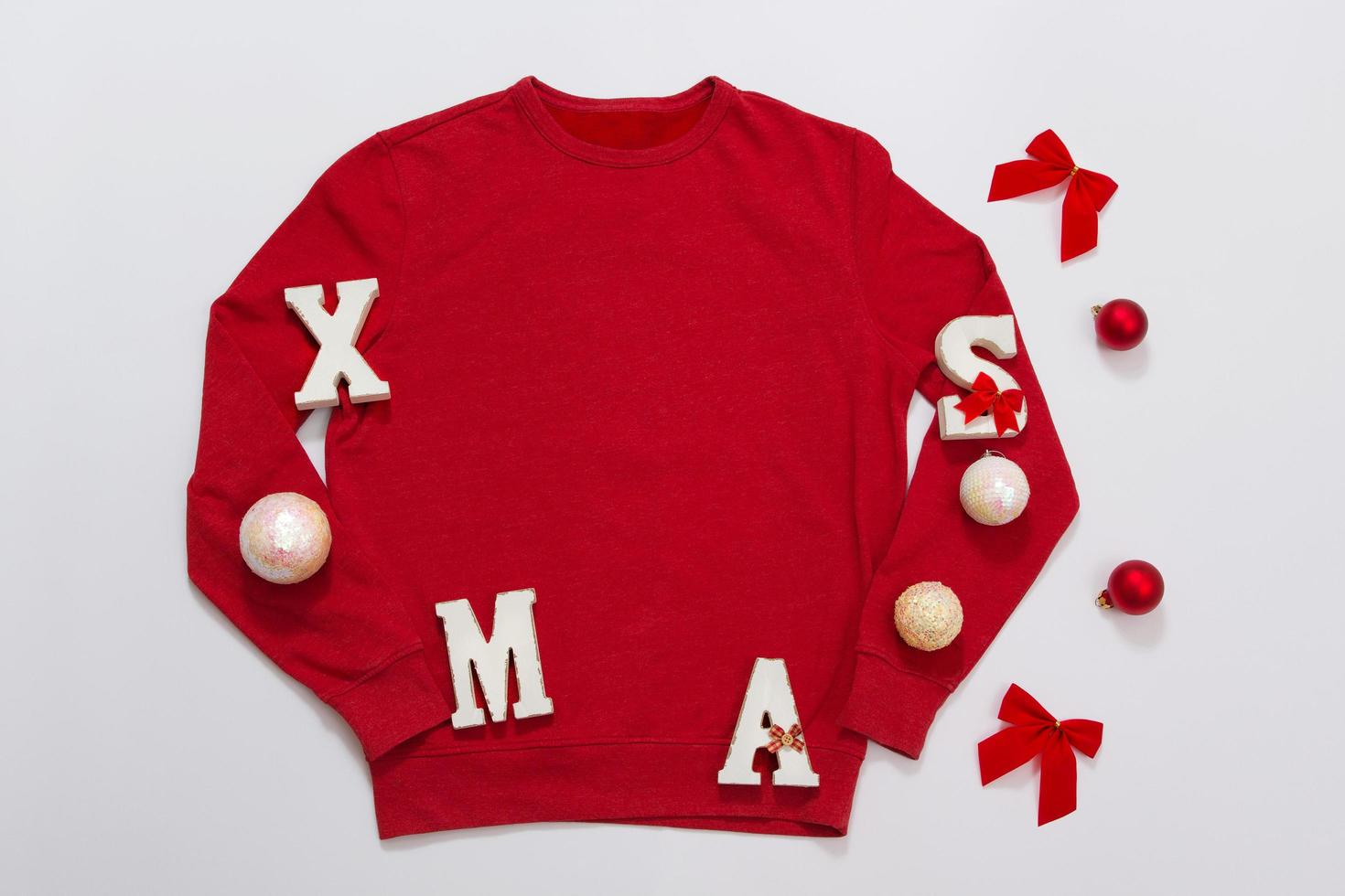 Close up red blank template sweatshirt with copy space and Christmas Holiday concept. Top view mockup hoodie and red holidays decorations on white background. Happy New Year accessories. Xmas outfit photo