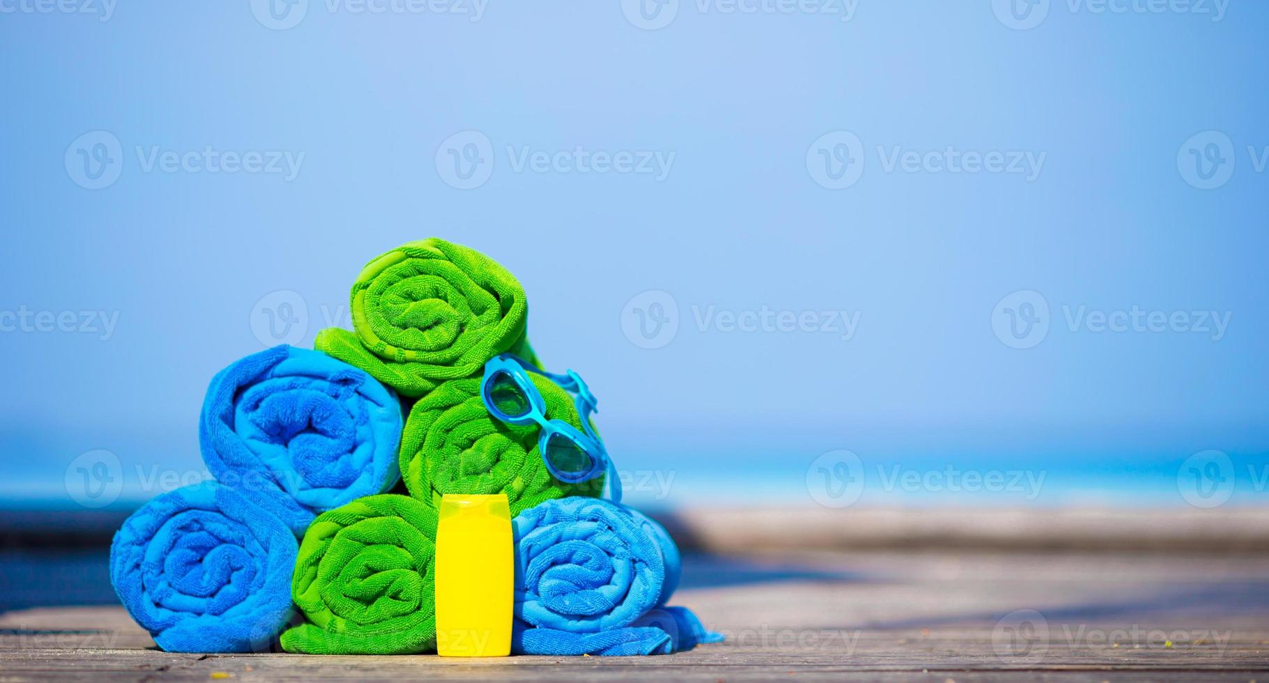 Beach and summer vacation accessories concept - close-up of colorful towels, swimming goggles and sunblock photo