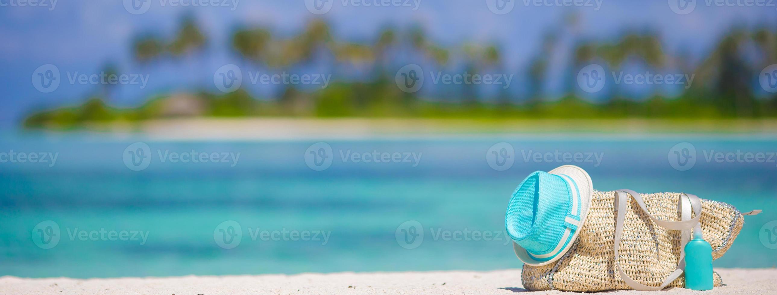 Straw bag, blue hat, sunglasses and sunscreen bottle on tropical beach photo