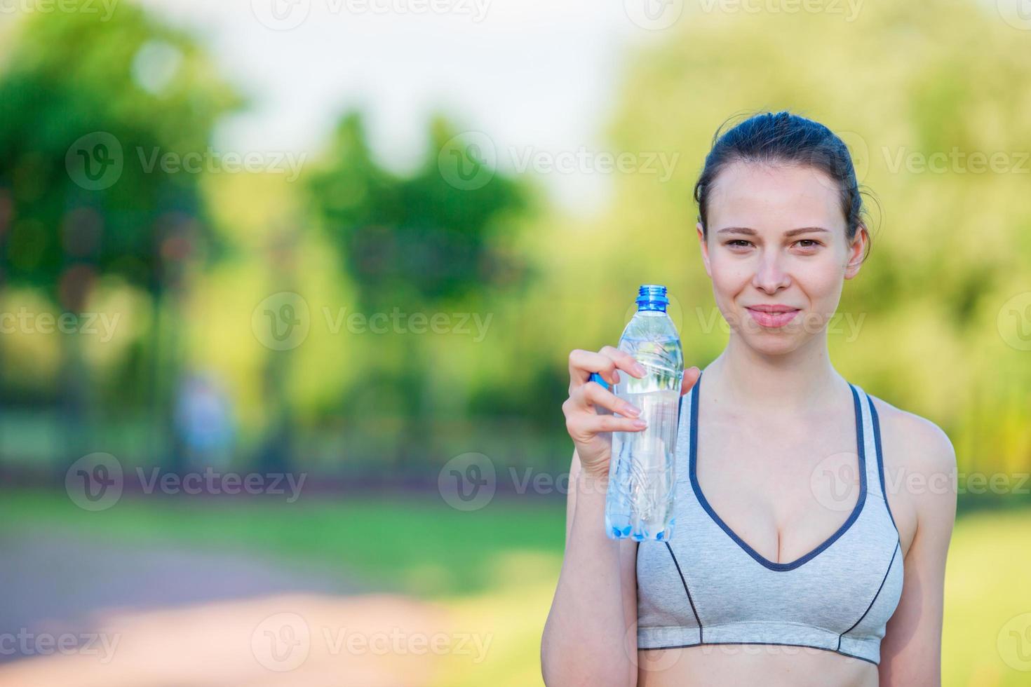 mujer joven con botella de agua después de correr afuera. modelo de fitness femenino entrenando afuera en el parque. estilo de vida de fitness de bienestar saludable. foto