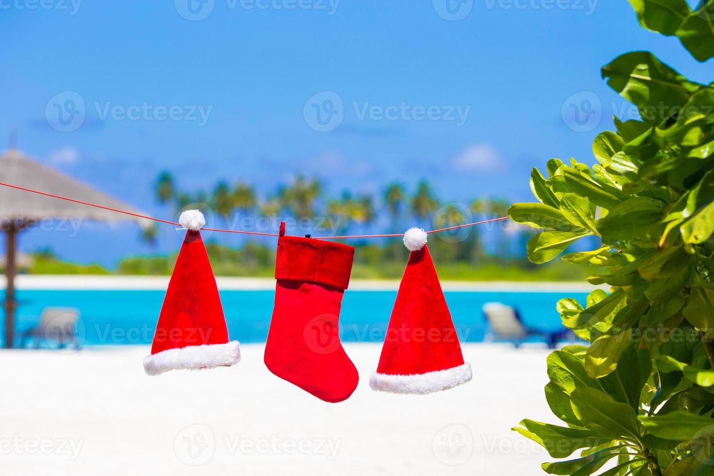 Red Santa hats and Christmas stocking hanging on tropical beach photo