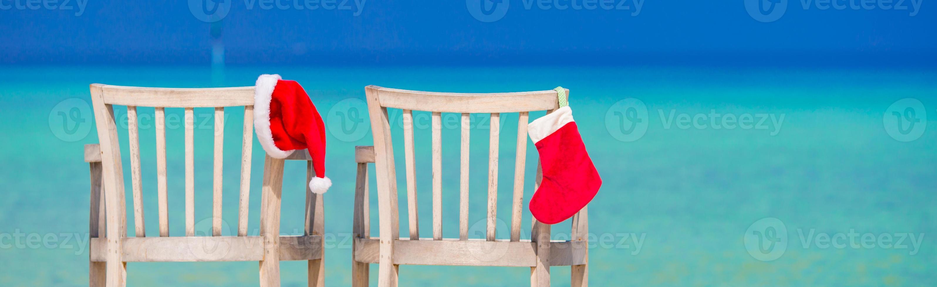 calcetín de navidad rojo y gorro de Papá Noel en una silla en la playa blanca tropical foto