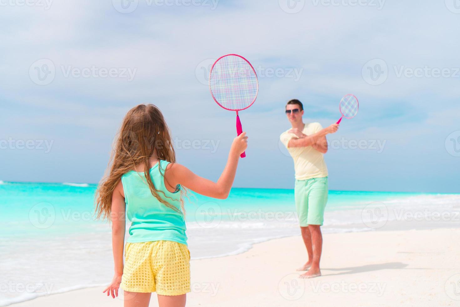 Little girl playing beach tennis on vacation with dad photo