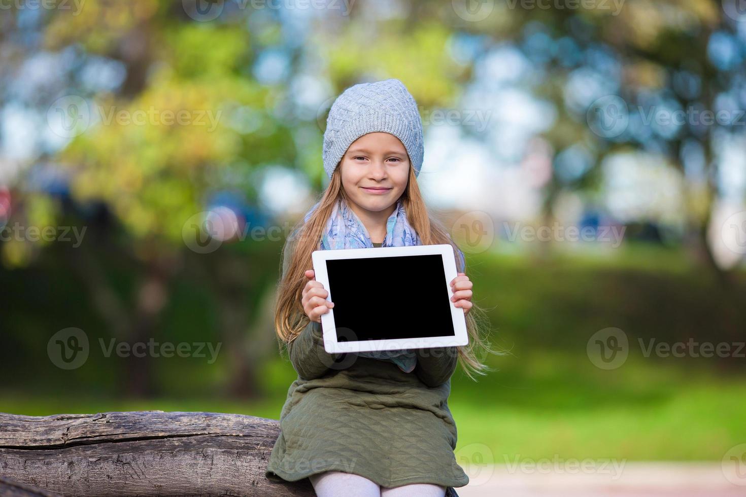 Adorable little girl holding tablet PC outdoors in autumn sunny day photo