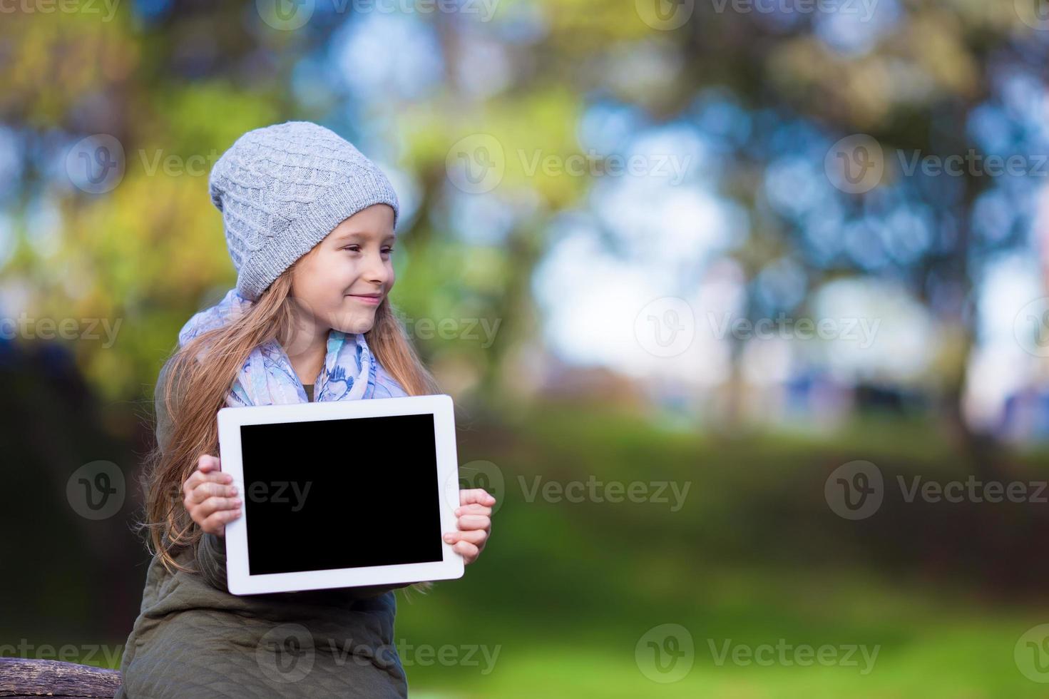 Adorable little girl holding tablet PC outdoors in autumn sunny day photo