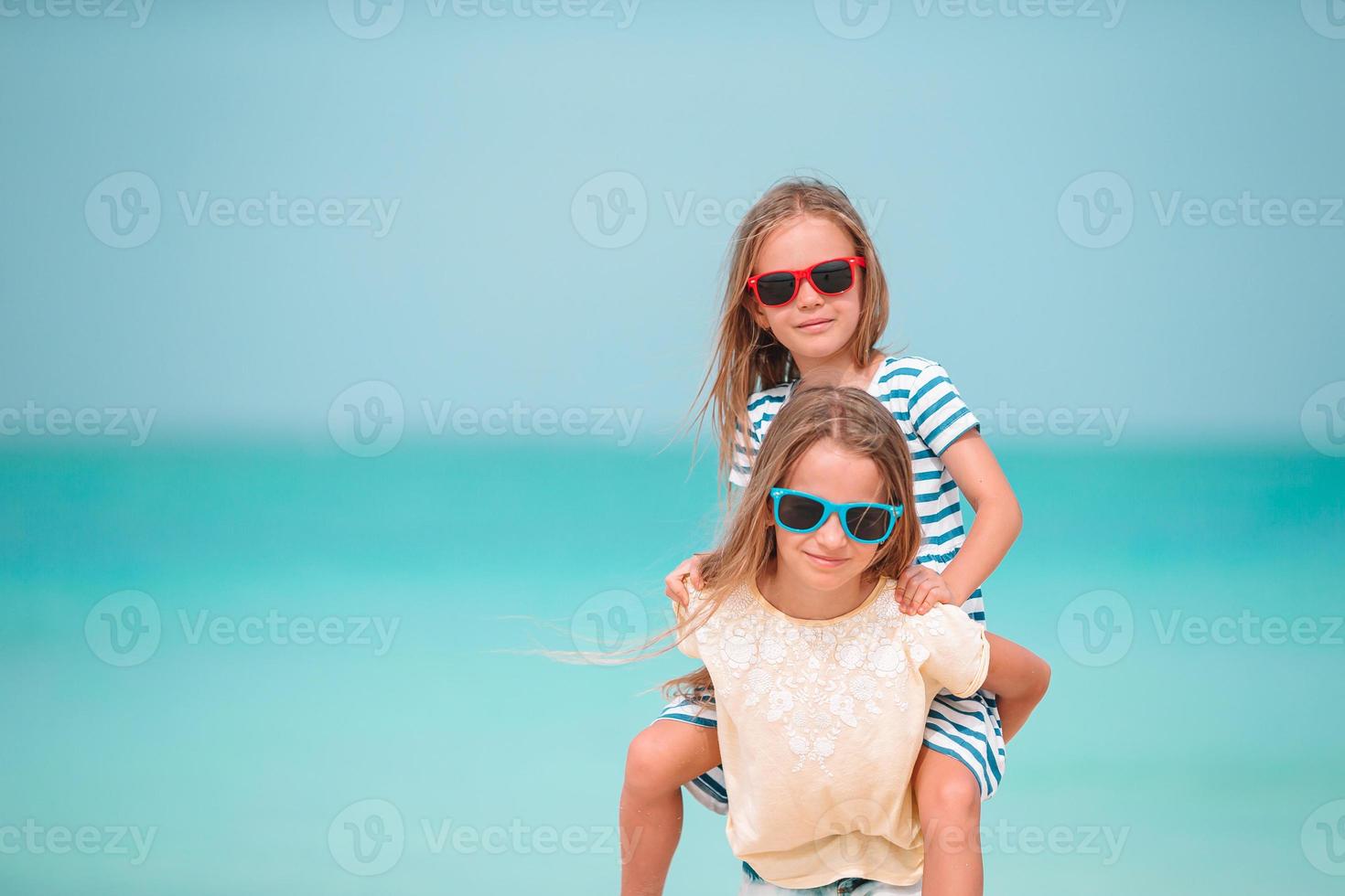 Little happy funny girls have a lot of fun at tropical beach playing together. Sunny day with rain in the sea photo