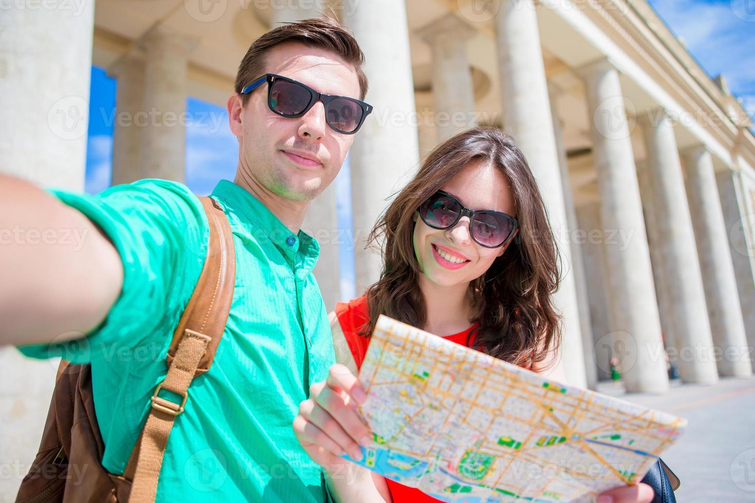 Young tourist friends traveling on holidays in Europe smiling happy. Caucasian family with city map making selfie background of attractions photo