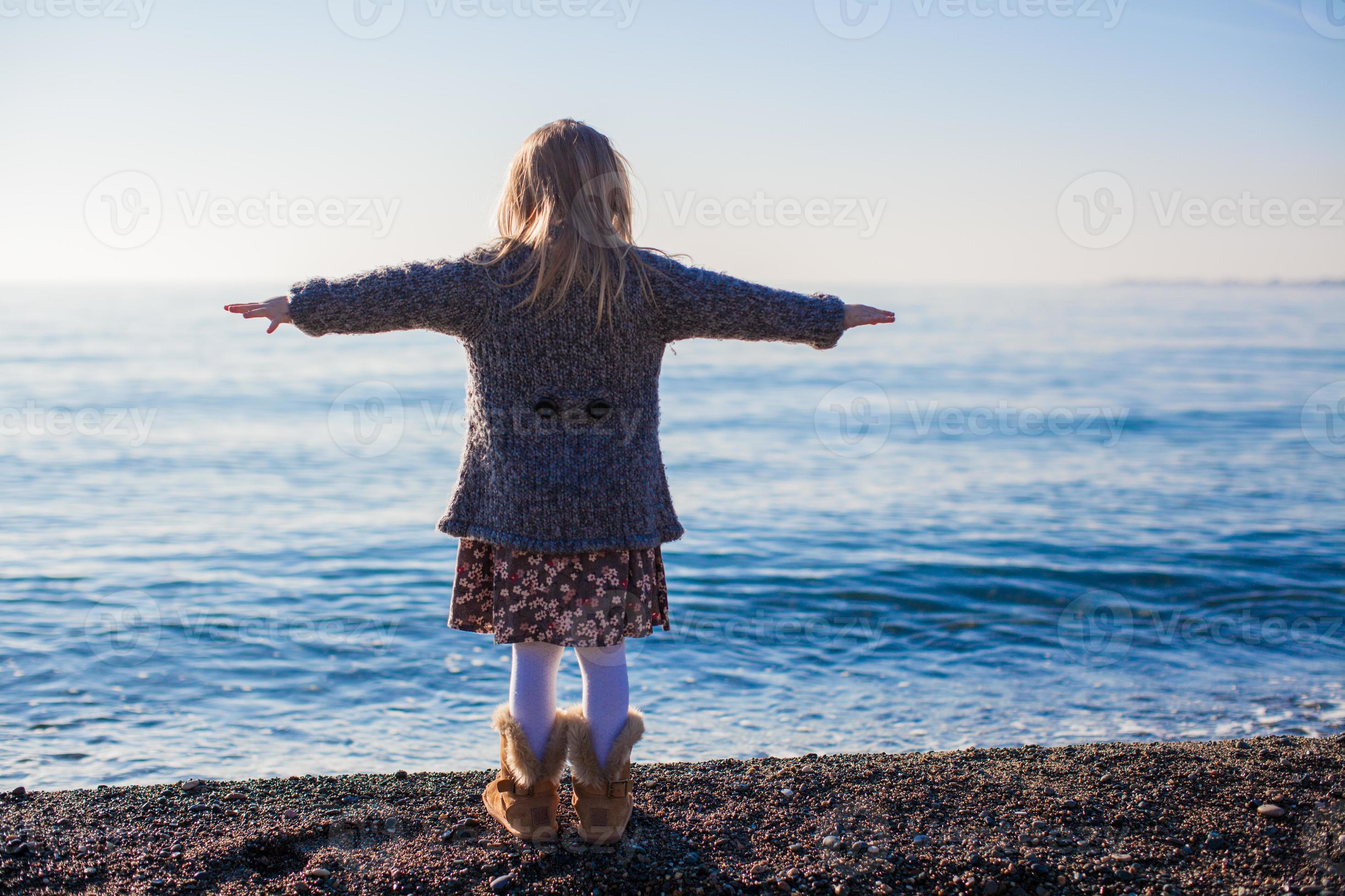 Rear view of little girl on the beach having fun at sunny winter day