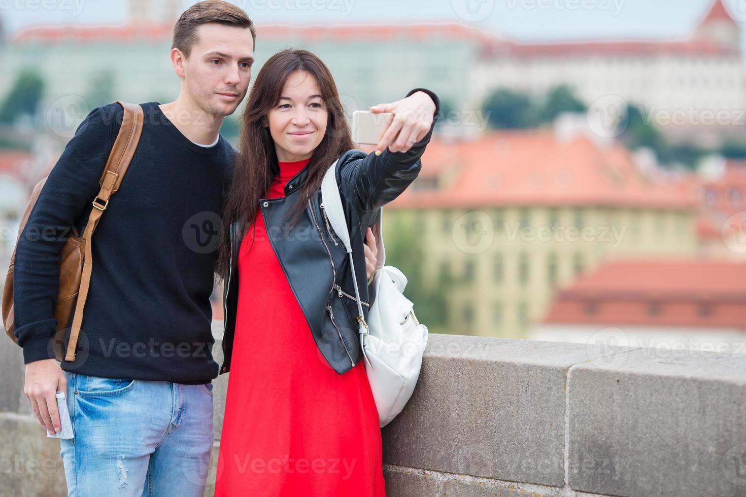 pareja joven que viaja de vacaciones en europa sonriendo feliz. familia caucásica haciendo selfie en popular karlov most foto
