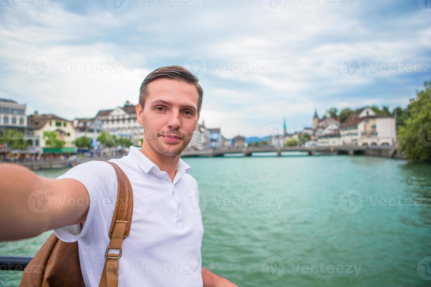 joven tomando selfie antecedentes famosa iglesia fraumunster y río limmat, suiza. foto