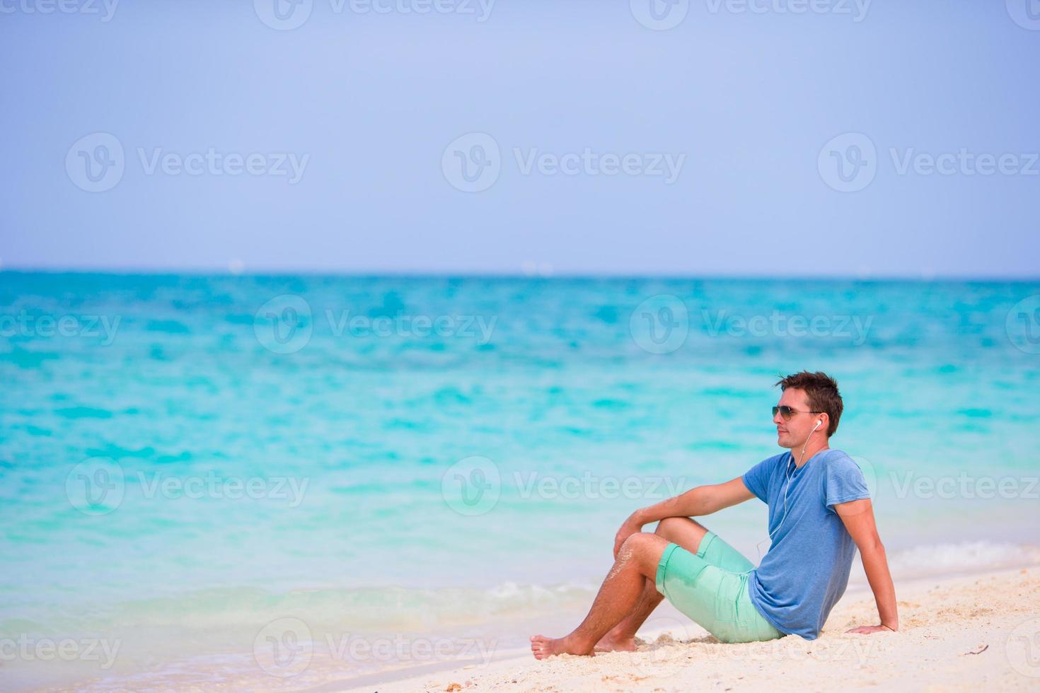 Young man enjoying the music on white sandy beach. Happy tourist relaxing on summer tropical vacation. photo