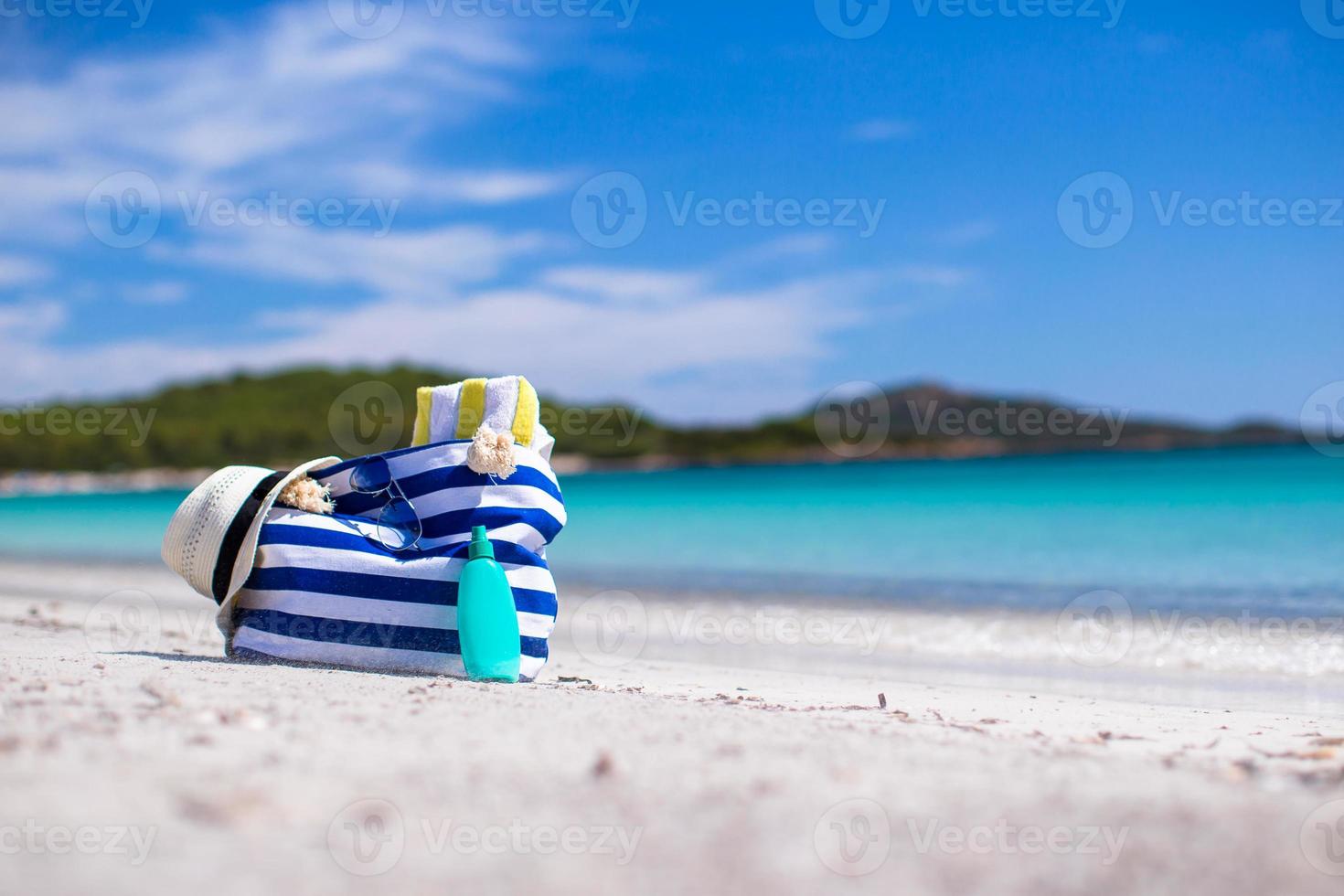 Stripe bag, straw hat, sunblock and towel on white tropical beach photo