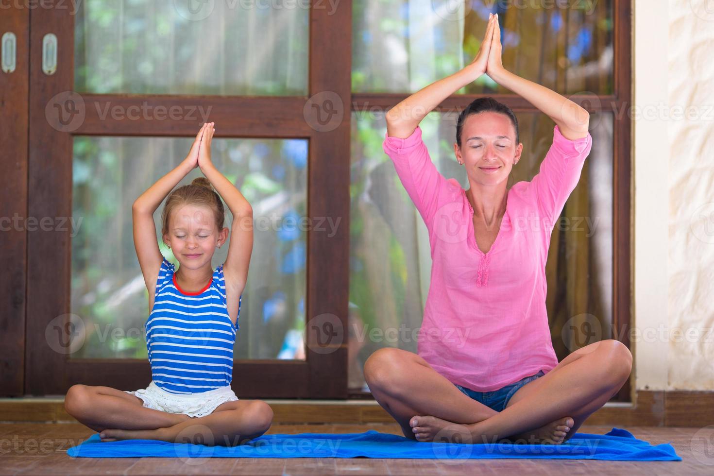 Young woman and little girl doing yoga exercise outdoor on terrace photo